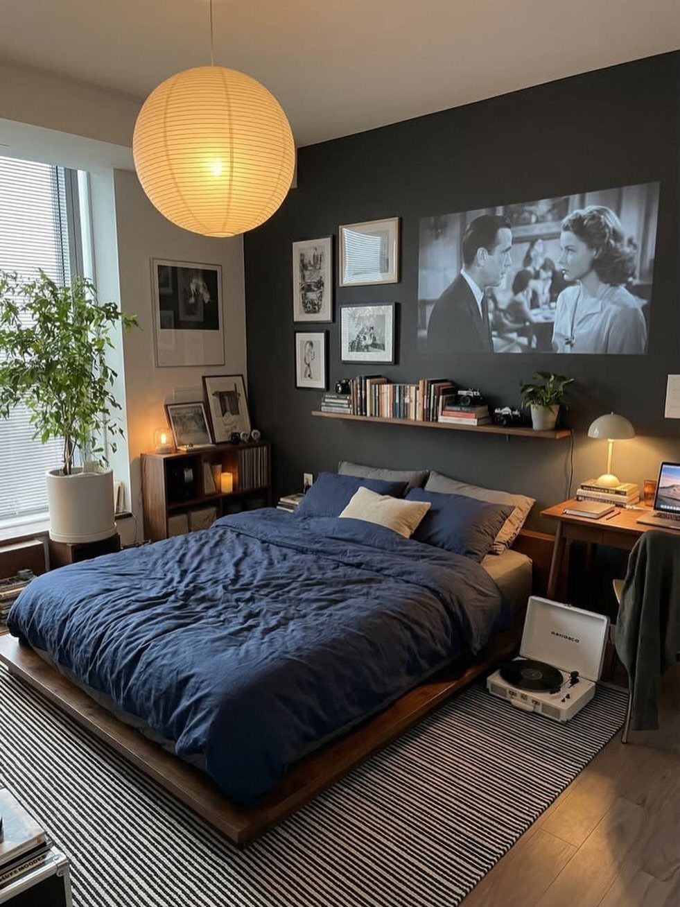 Bedroom with navy blue bedding and a dark charcoal accent wall and wooden furniture.