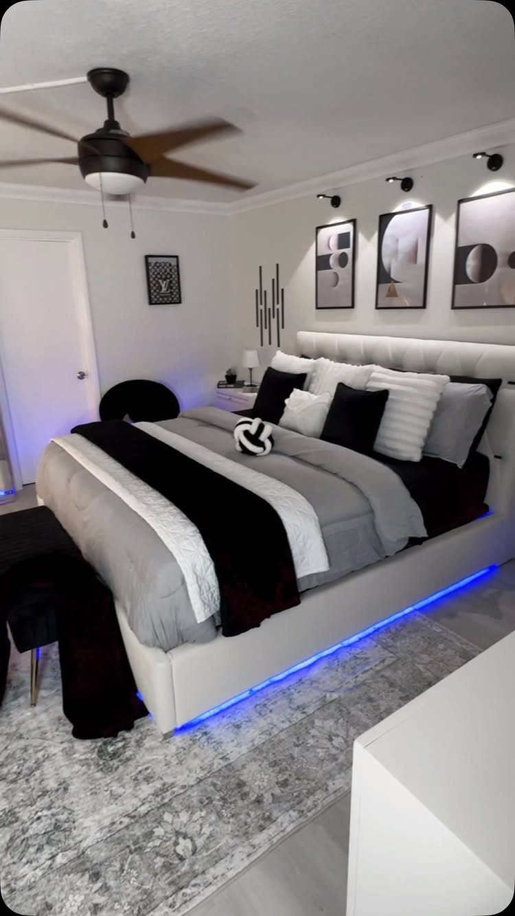 Modern bedroom with white bed, black and grey bedding, and blue LED lighting.