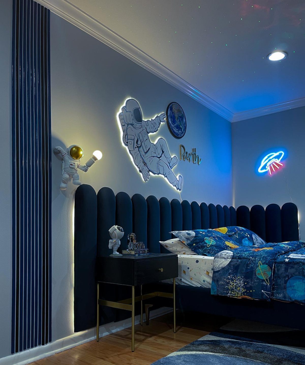 Space-themed bedroom with navy blue headboard and black nightstand with gold metal legs.