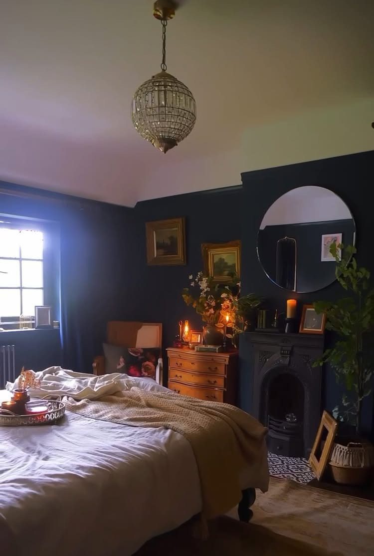 Navy blue bedroom with a white bed, wooden dresser, and black fireplace.