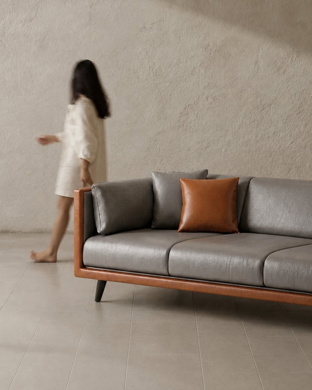 Leather Sofa Living Room Ideas: 8 Styles and Layouts 6 Grey leather sofa with brown pillow in a minimalist room with a blurred woman