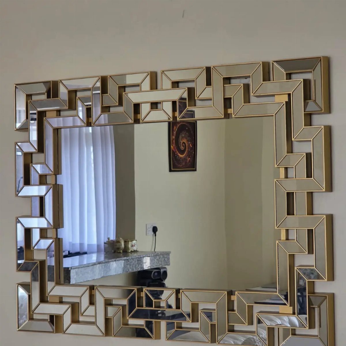Large rectangular mirror with a gold geometric frame mounted on a neutral wall.