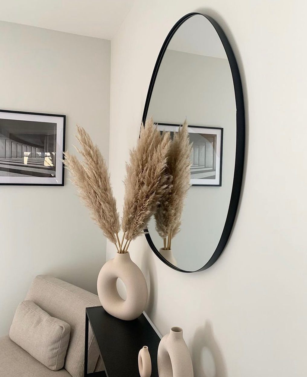 Pampas grass in a donut vase on a black console table with oval mirror.
