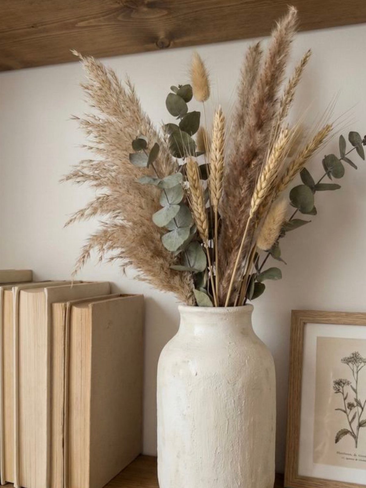 White ceramic vase with pampas grass and eucalyptus on a wooden shelf.
