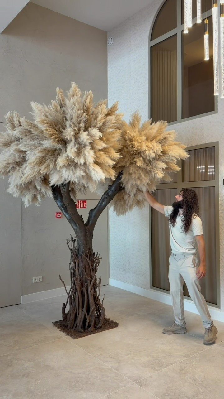 Man standing by a large artificial tree with fluffy beige pampas grass canopy.